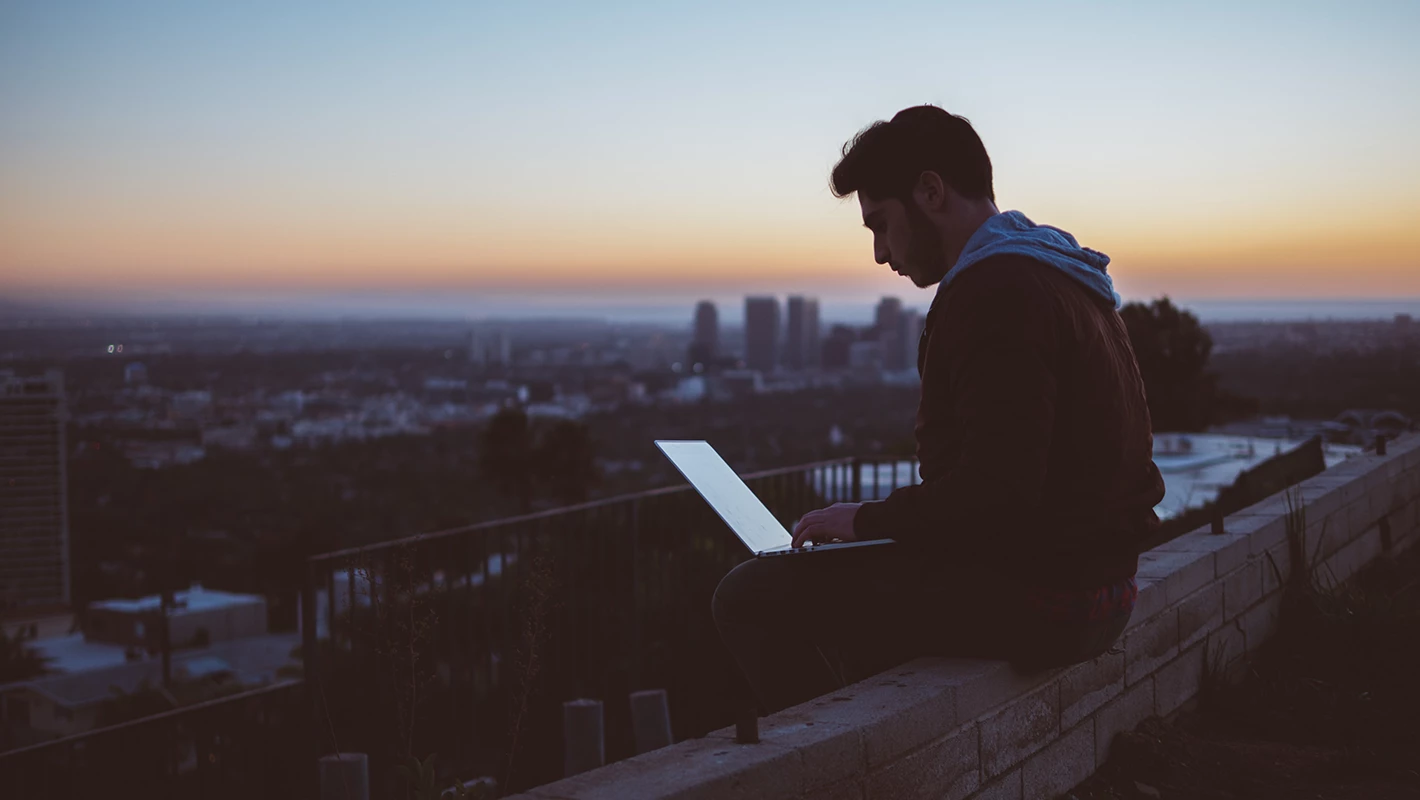 Person mit Laptop vor einer Skyline bei Sonnenaufgang